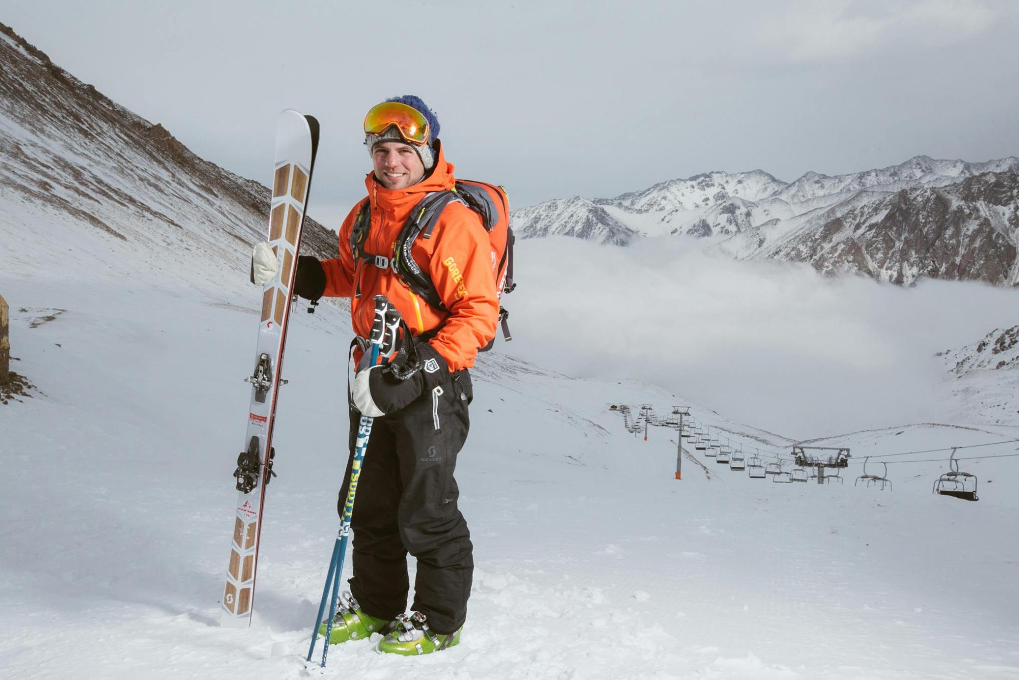 Man in Orange Holding Pair of Skis