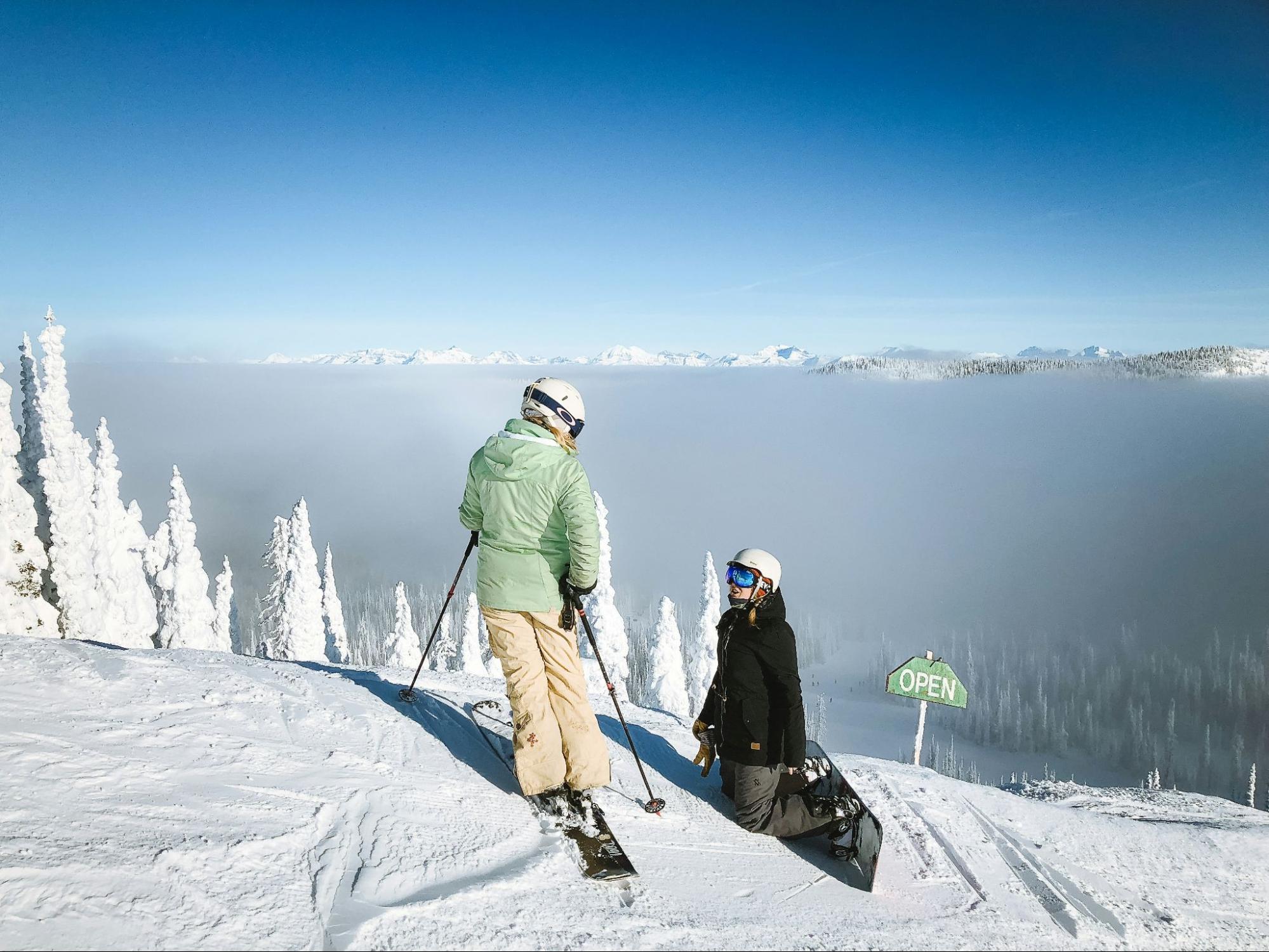 A skier and snowboarder at the top of a snowy slope.